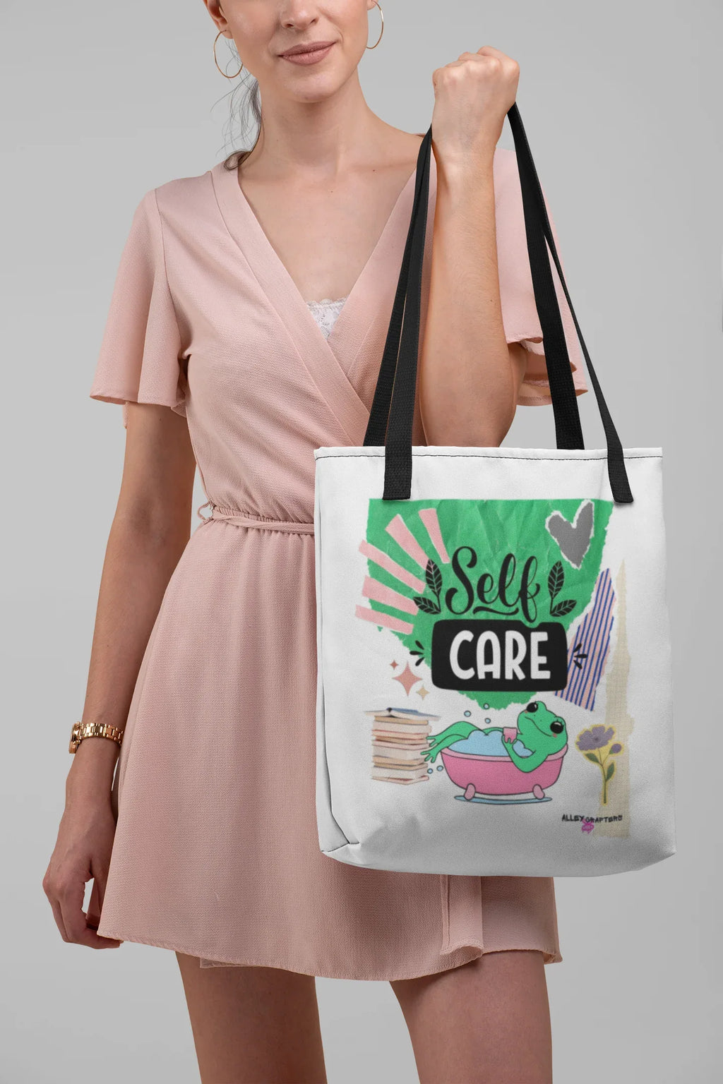White tote bag with green 'Self Care' frog graphic, black shoulder handles