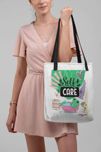 White tote bag with green 'Self Care' frog graphic, black shoulder handles