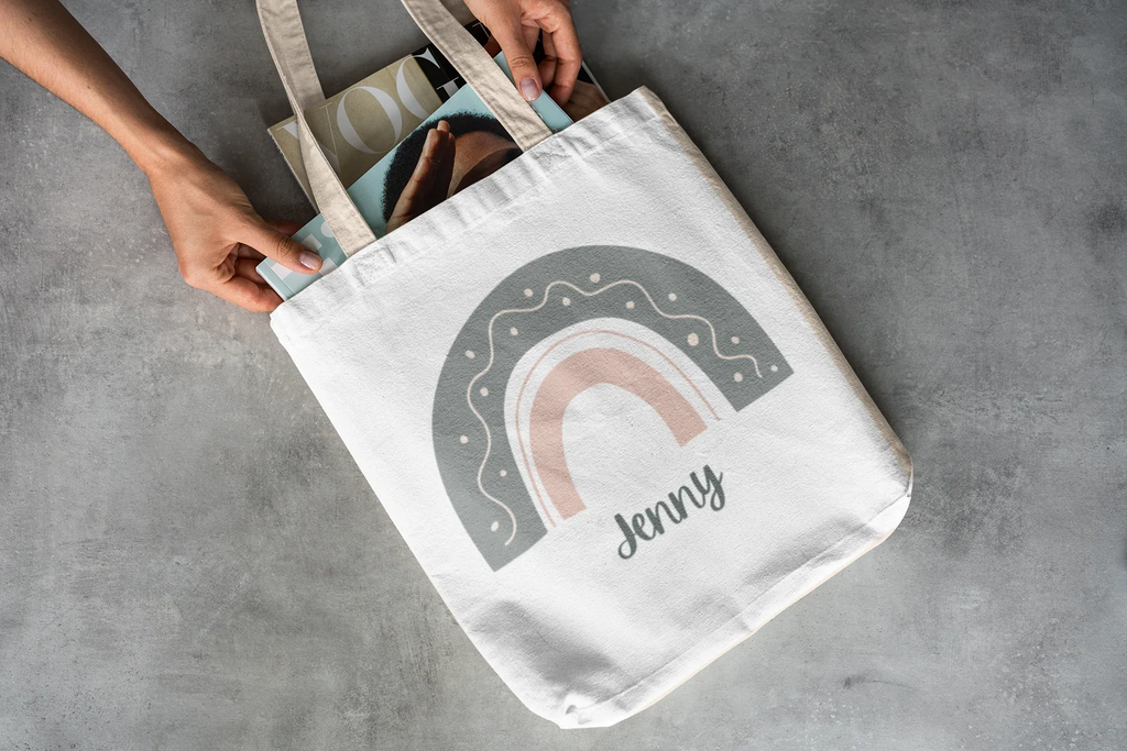 White tote bag in hand with rainbow arch graphic and name Jenny