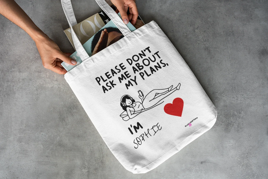 White canvas tote bag with black straps and quote print: “Please don’t ask me about my plans”