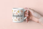 White mug with geometric triangles and name Sophie, held by a hand