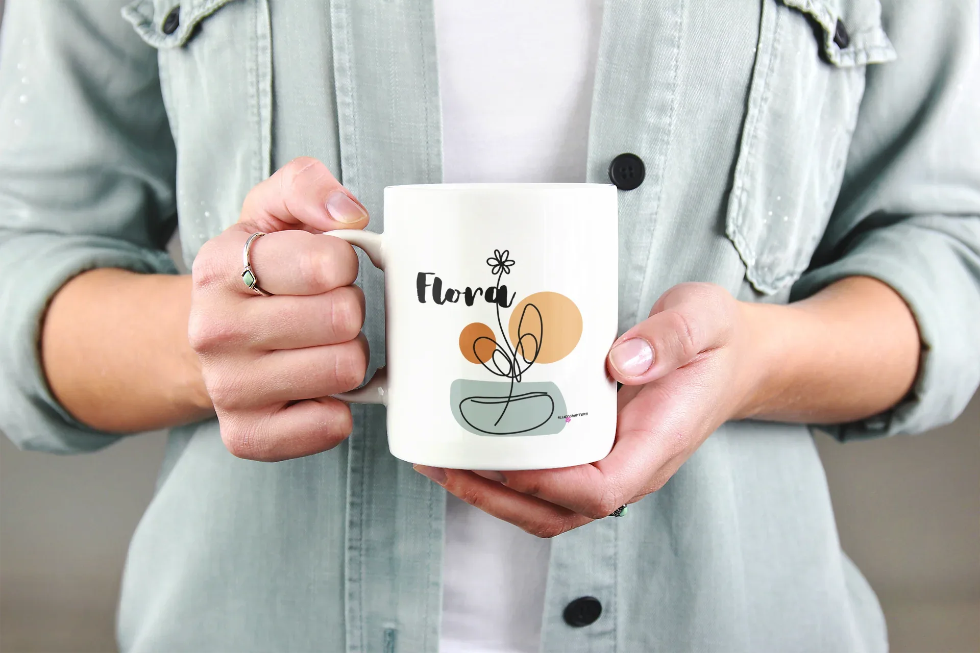 White ceramic mug with Flora name and floral pot graphic, held in hands