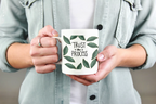 White coffee mug with green leaf wreath and “Trust the Process” held in hands