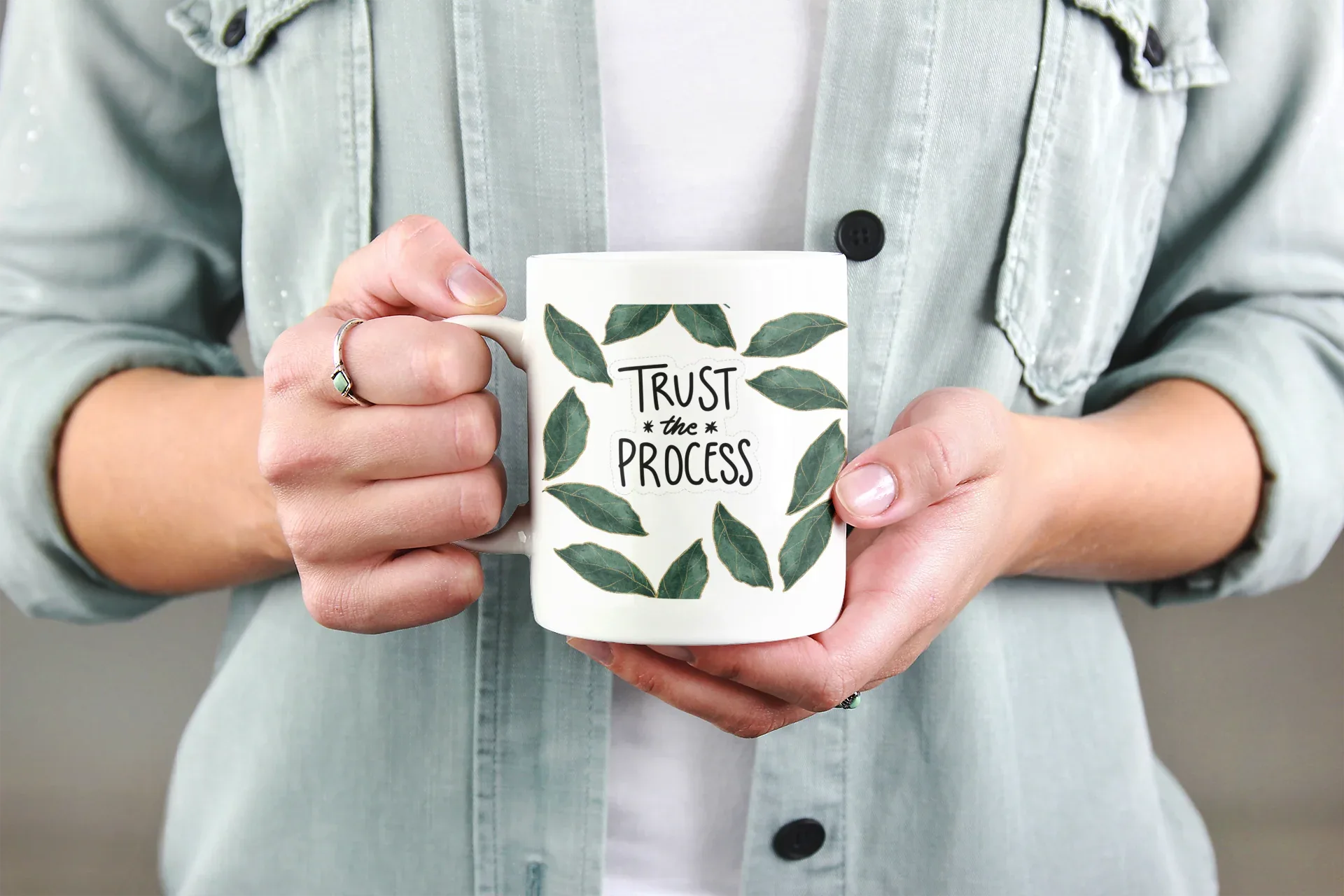 White coffee mug with green leaf wreath and “Trust the Process” held in hands