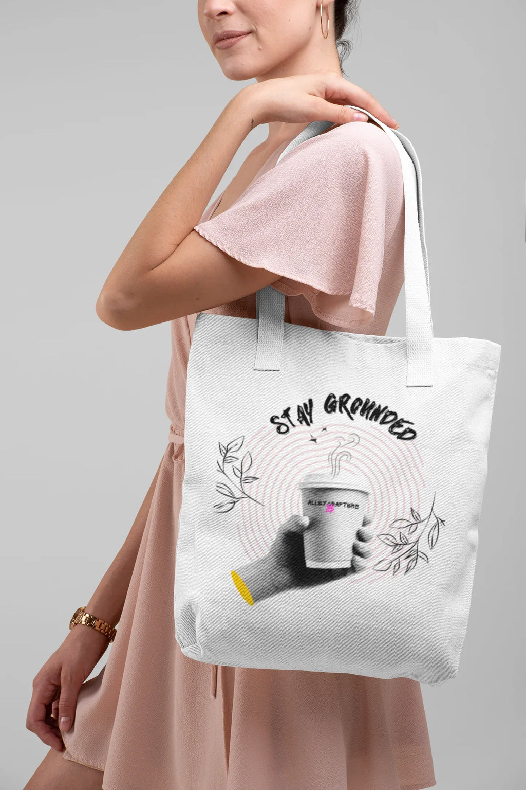 White canvas tote bag with pink handles and Stay Grounded coffee cup graphic on person