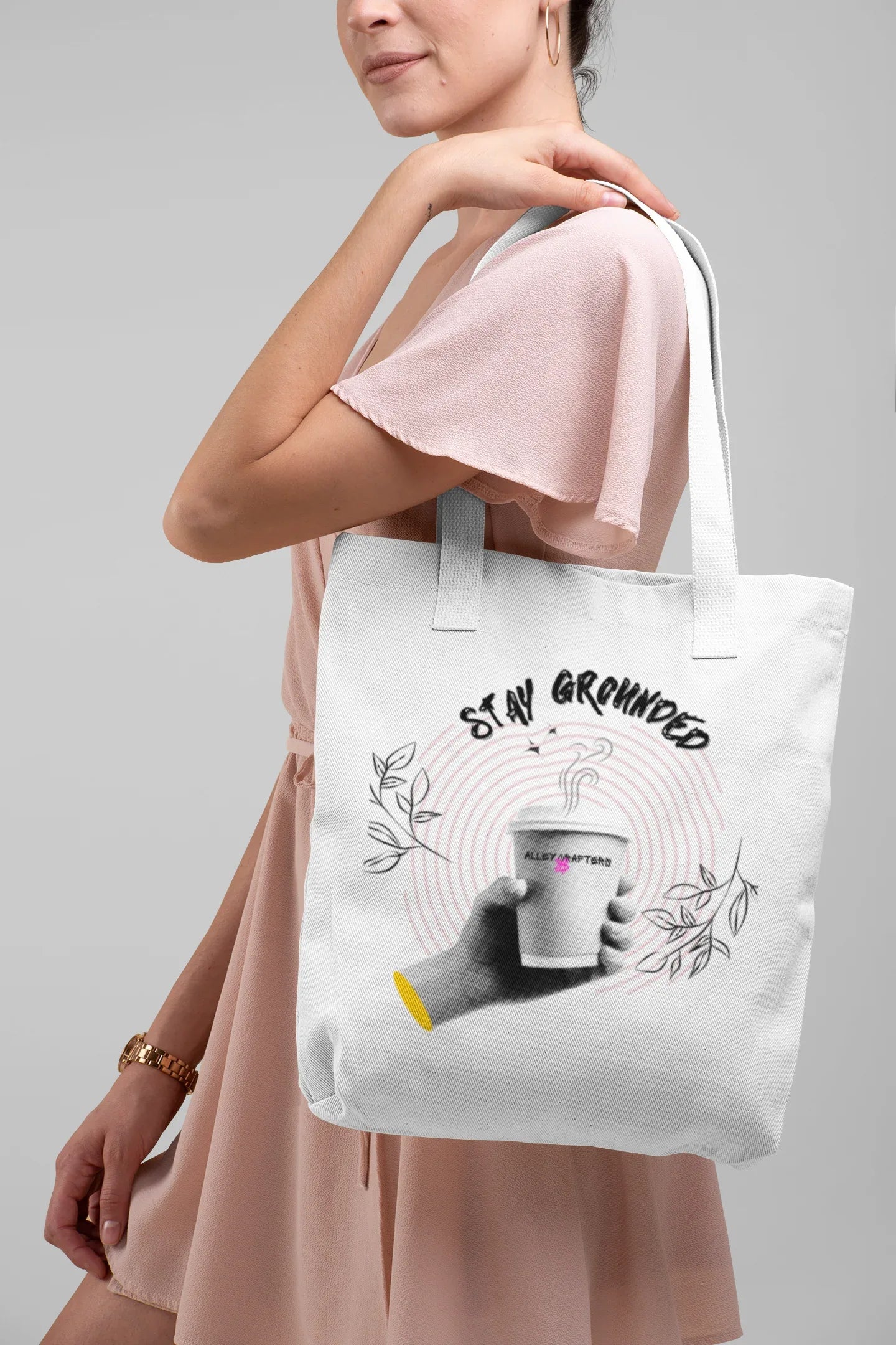 White canvas tote bag with pink handles and Stay Grounded coffee cup graphic on person