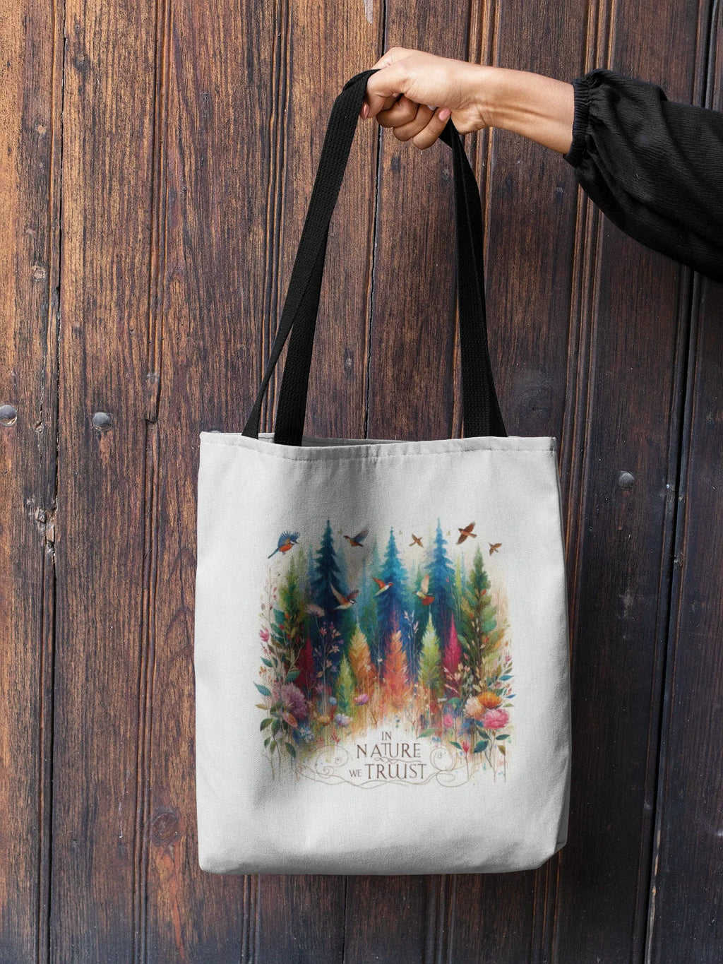 White tote bag with black handles, forest and birds print, held by hand at top handle