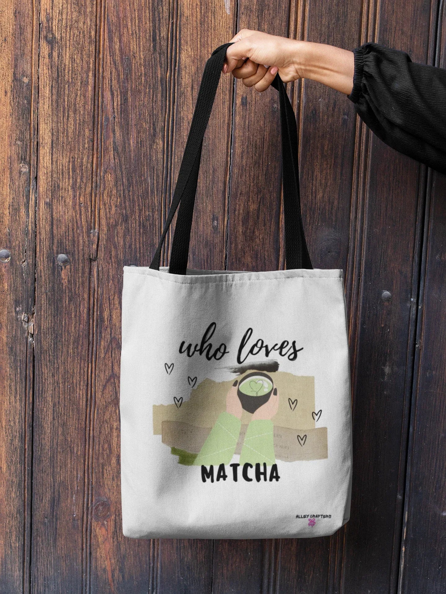 White tote bag with “who loves MATCHA” print, held by black top handles.