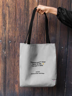 White canvas tote bag with black handles and front slogan text