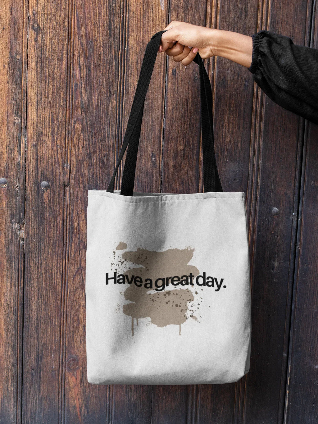 White tote bag held by top handles, brown 'Have a great day' print centered