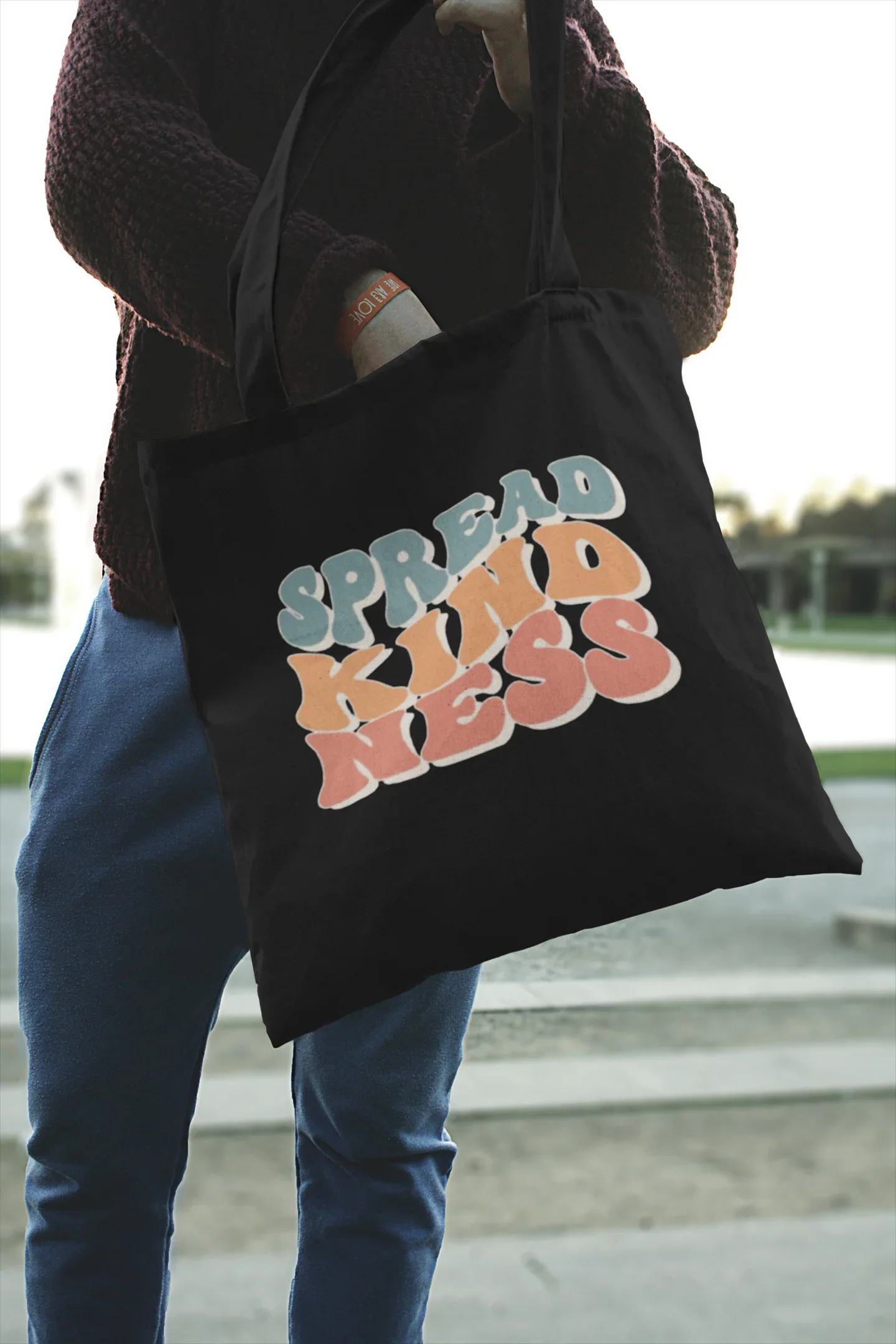 Black cotton tote bag with 'SPREAD KINDNESS' graphic, hanging from a person