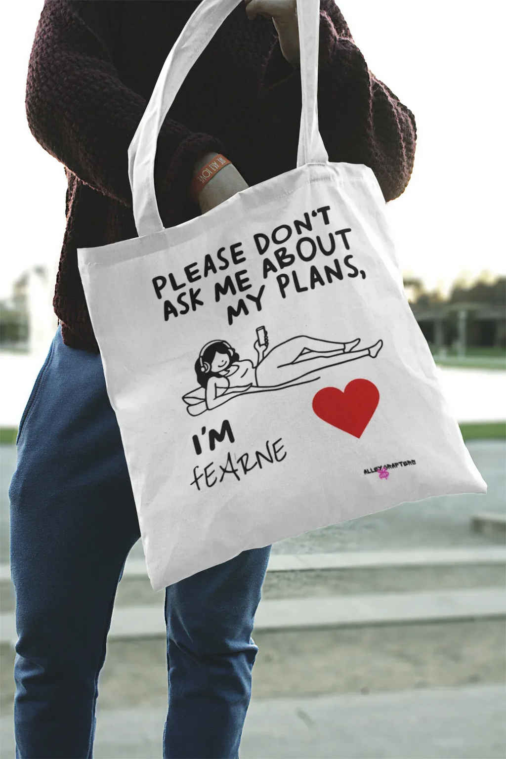 White canvas tote bag being carried, “Please don’t ask me about my plans” print and red heart