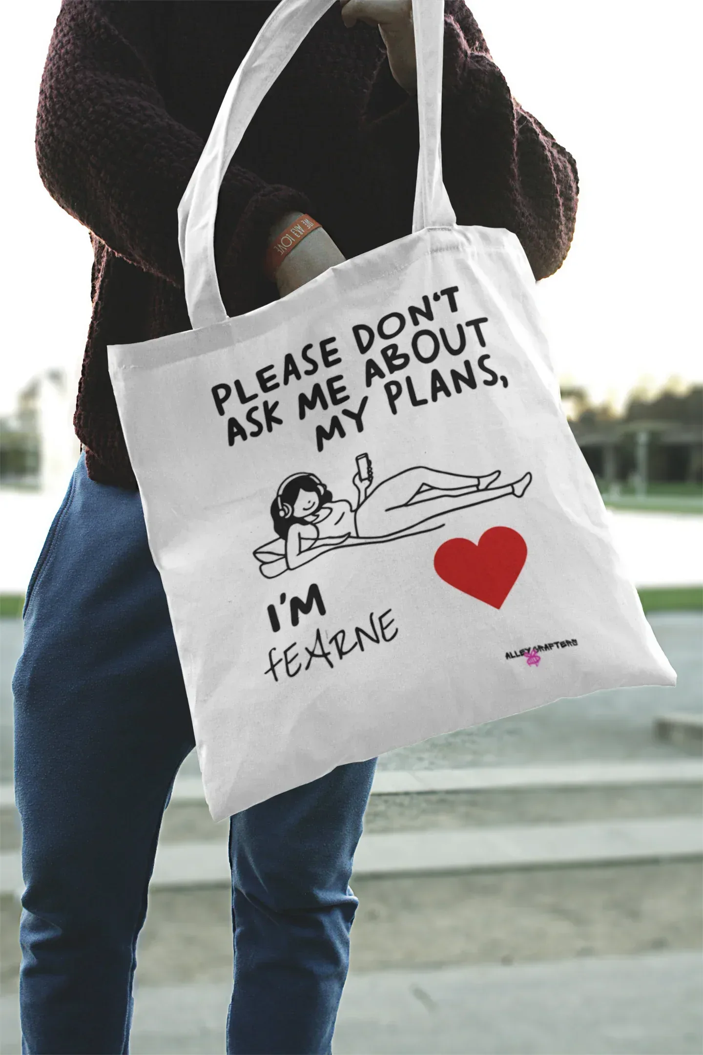 White canvas tote bag being carried, “Please don’t ask me about my plans” print and red heart