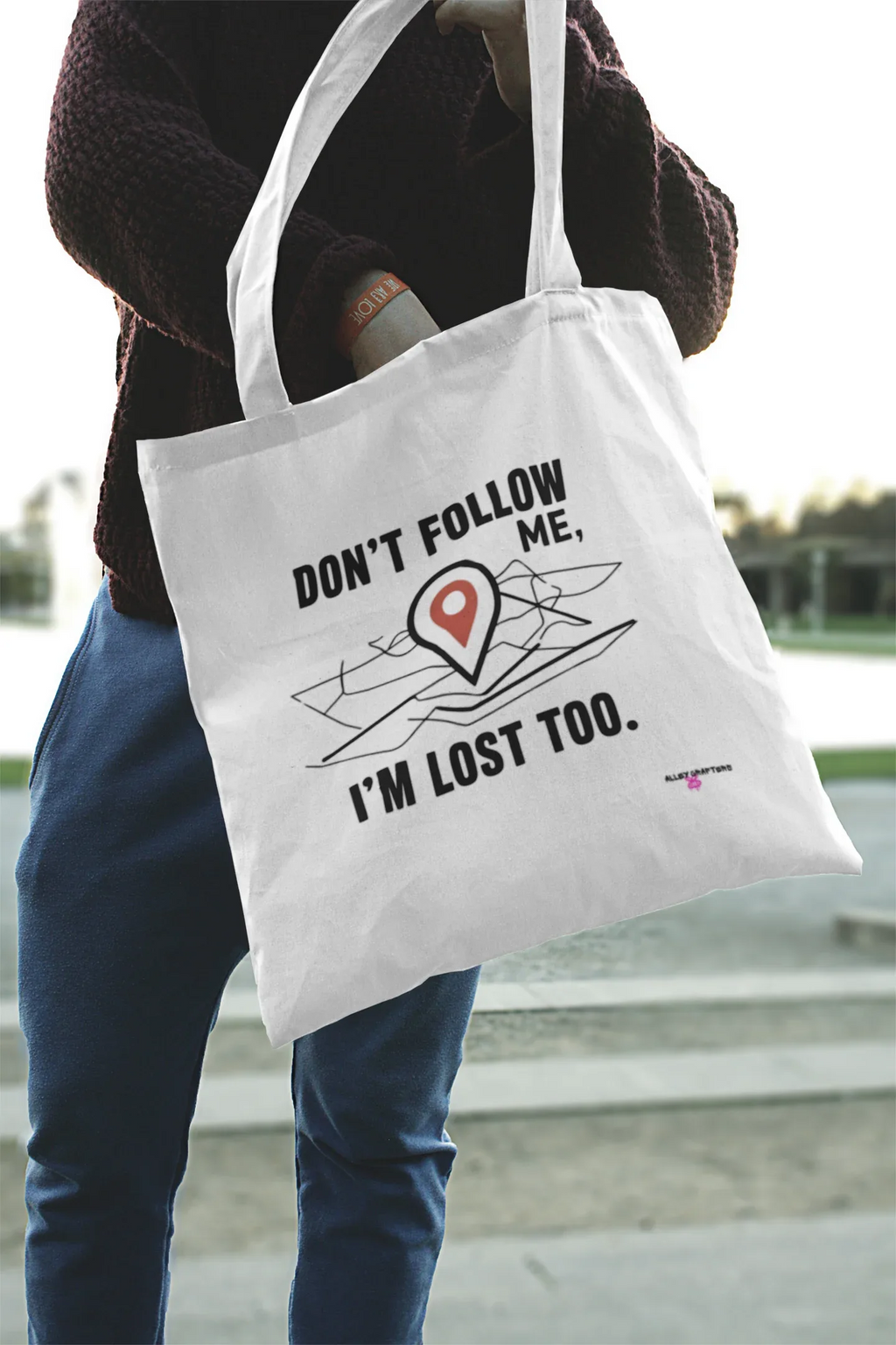 White canvas tote bag with black slogan "DON'T FOLLOW ME" and red location-pin graphic