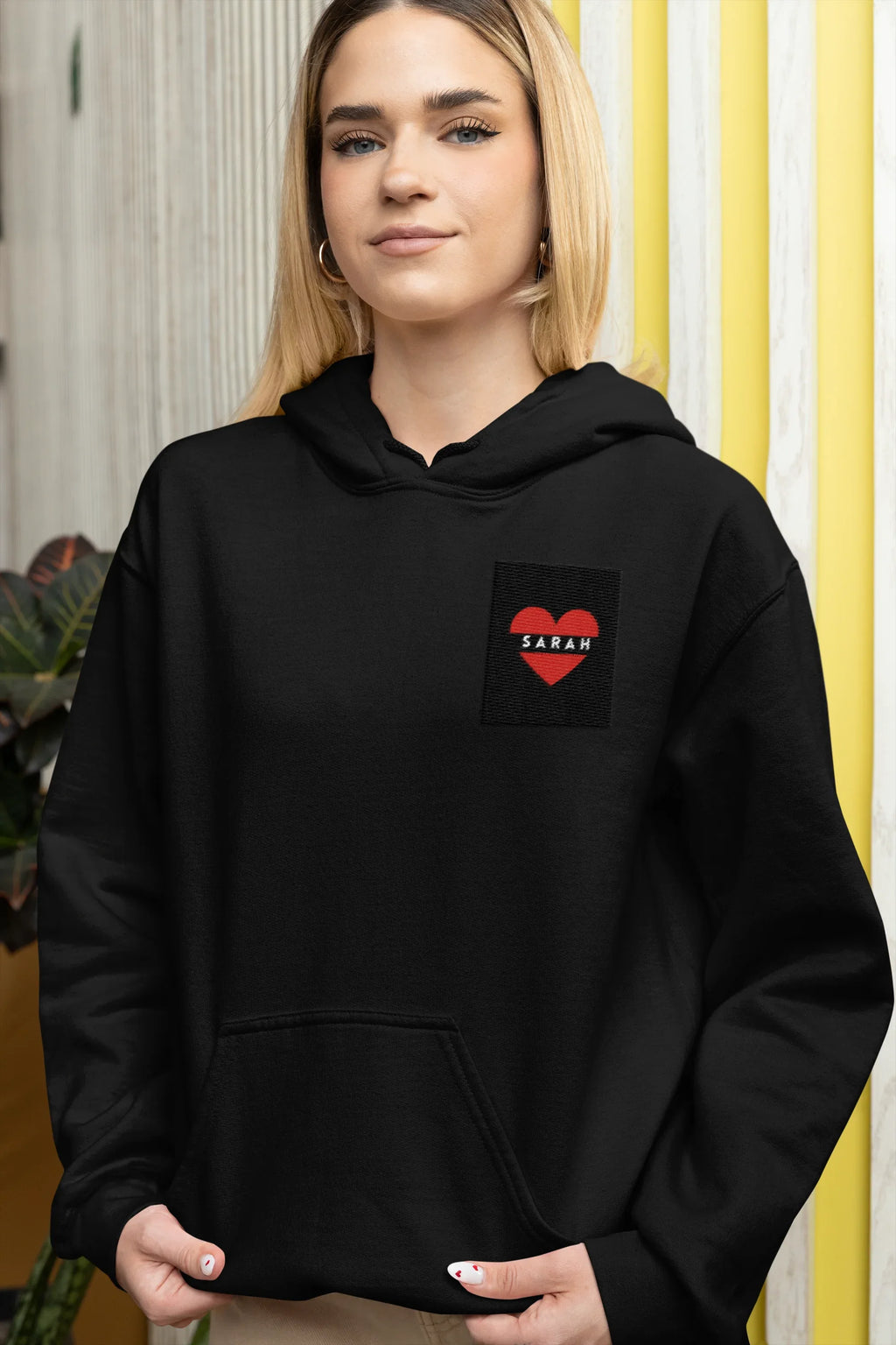 Black unisex hoodie with front pocket and heart embroidery patch reading SARAH