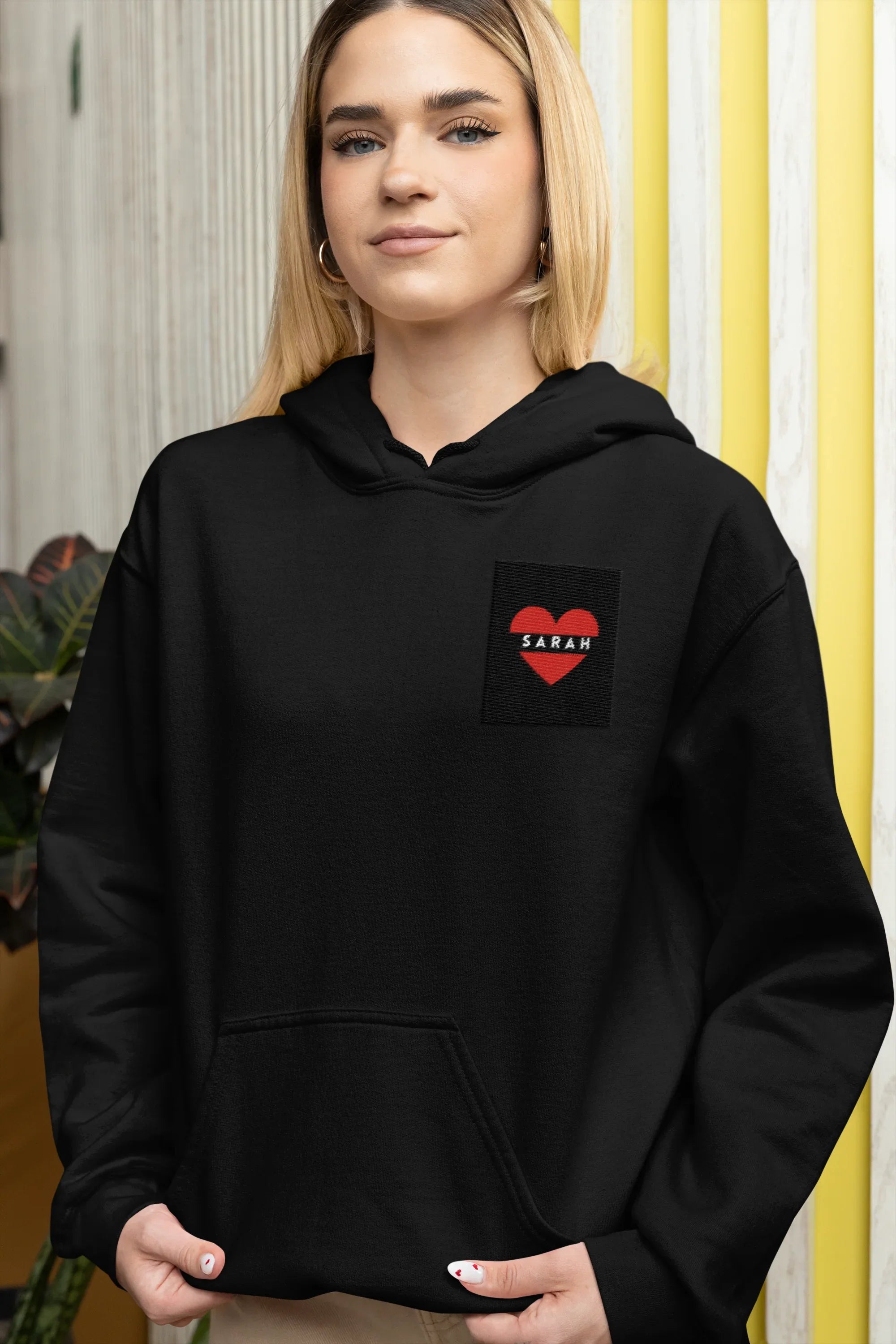 Black unisex hoodie with front pocket and heart embroidery patch reading SARAH