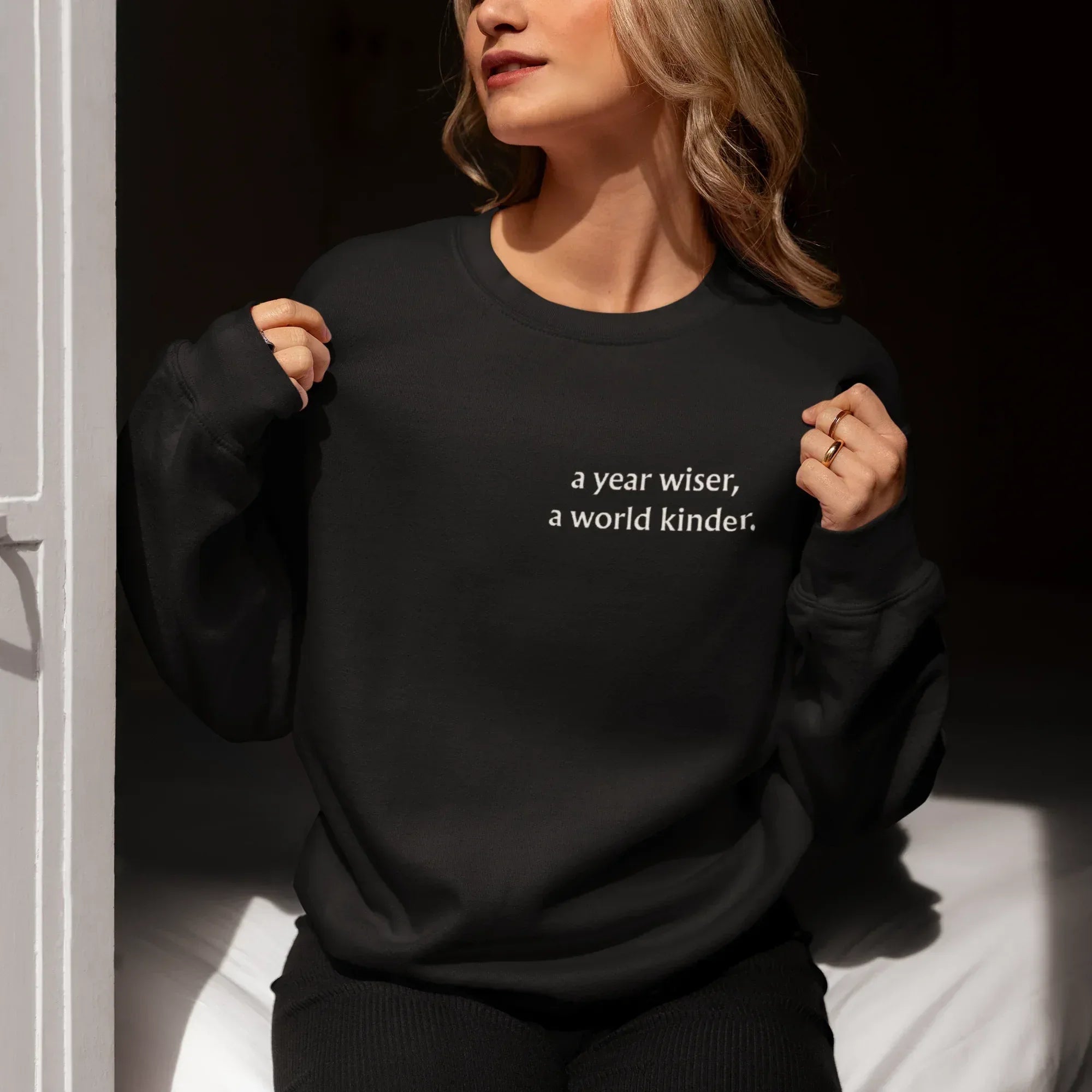 Black crewneck sweatshirt with a year wiser, a world kinder print