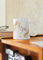 White mug with gold filigree corners and dark red 'T & M' design