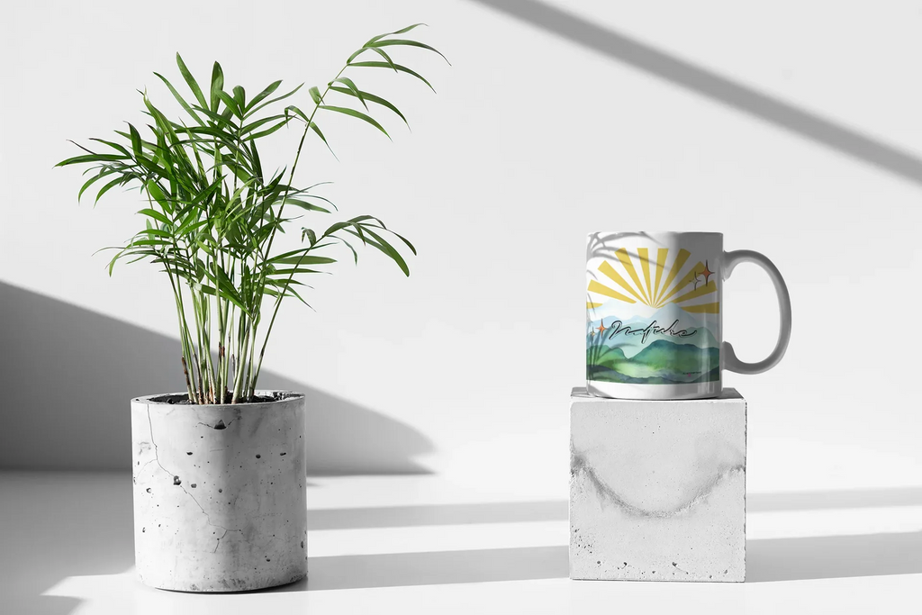 White coffee mug with sunrise rays and mountain landscape print on front