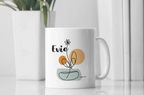 White ceramic mug with Evie name and floral swirl design on front, room setting.