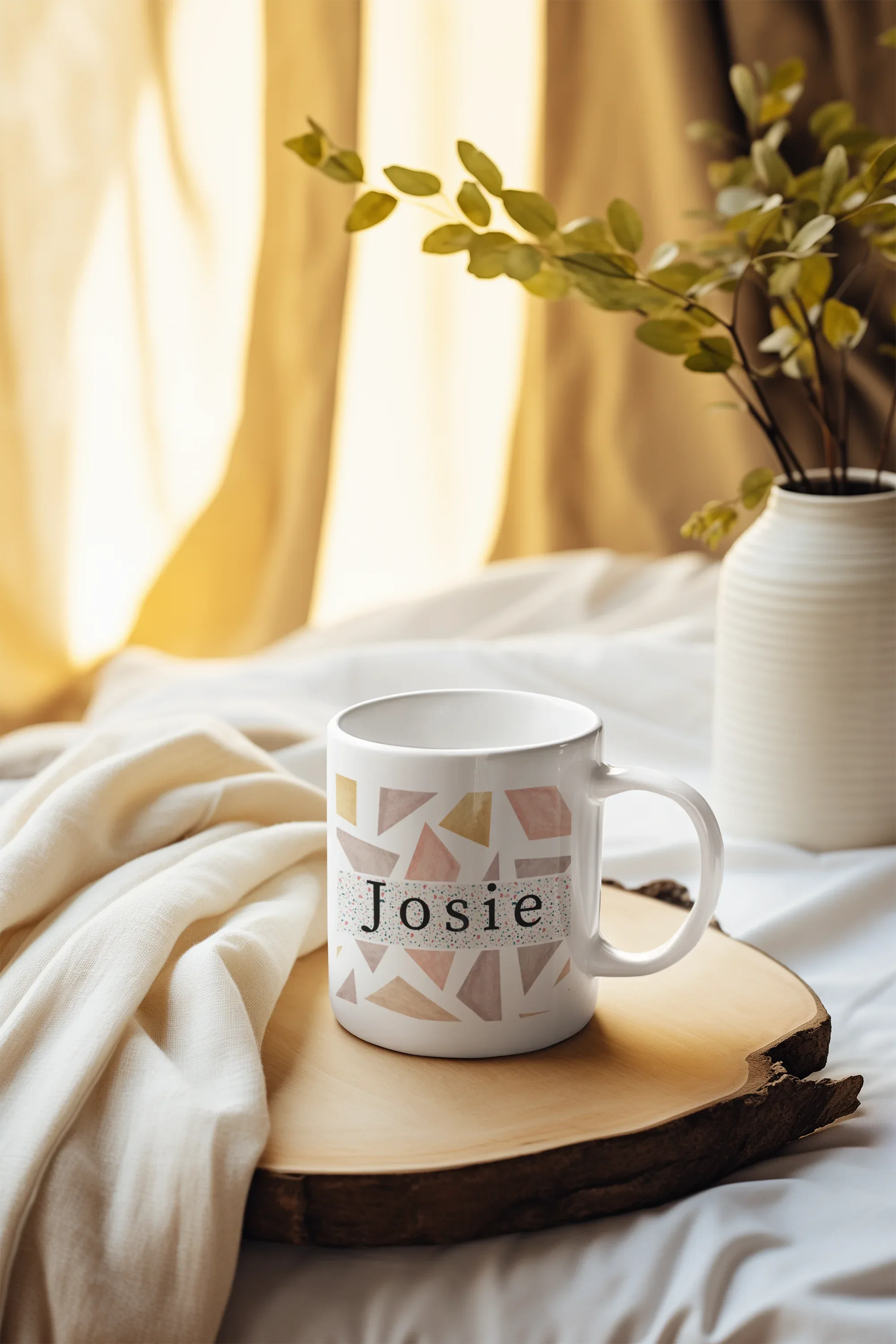 White mug with geometric triangles and name Josie on a wooden slice with cloth
