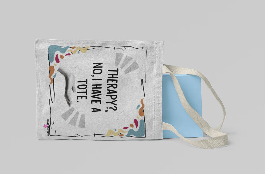 White tote bag with “Therapy?, No, I have a Tote” text, laid flat with light straps