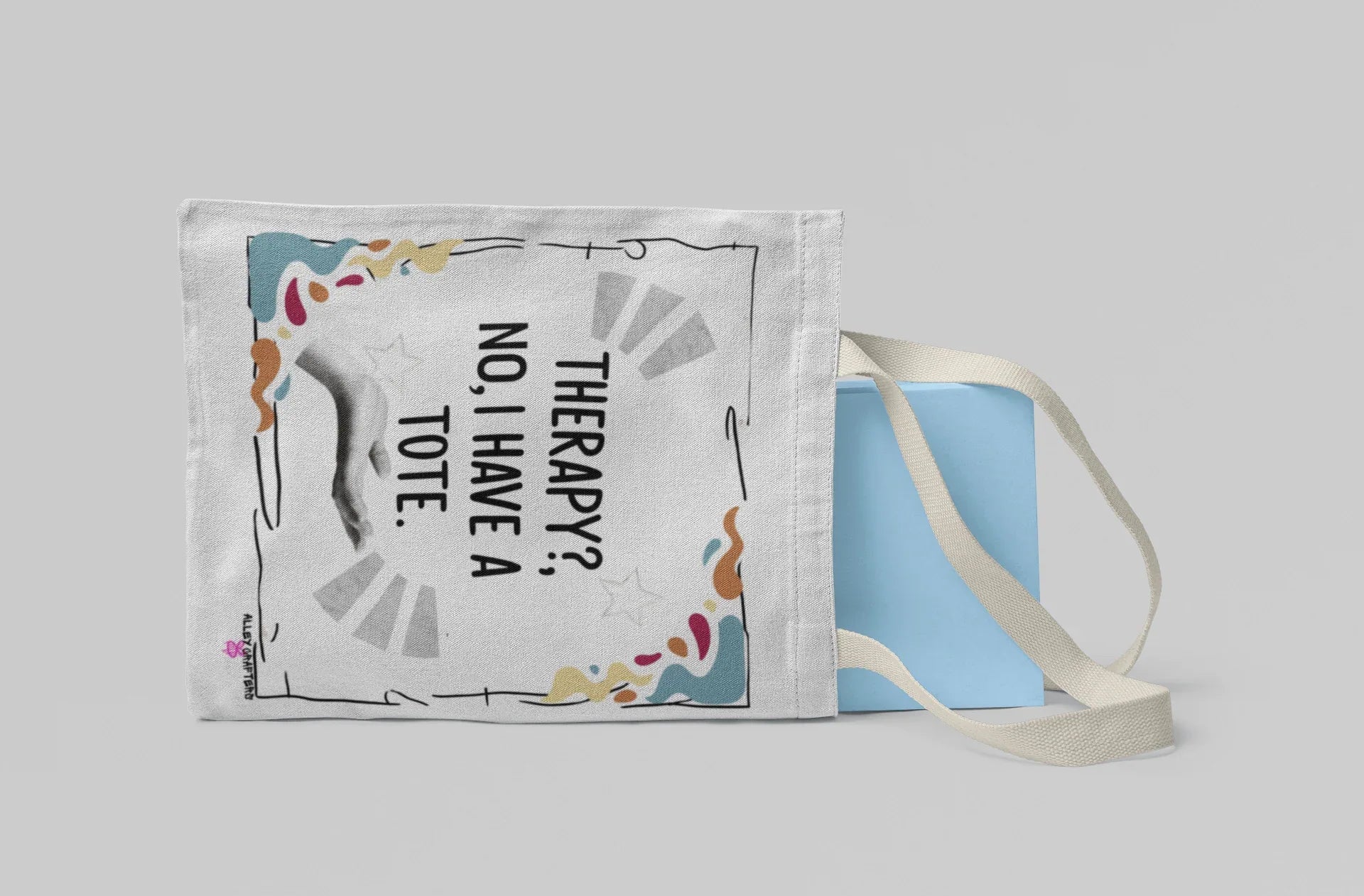 White tote bag with “Therapy?, No, I have a Tote” text, laid flat with light straps