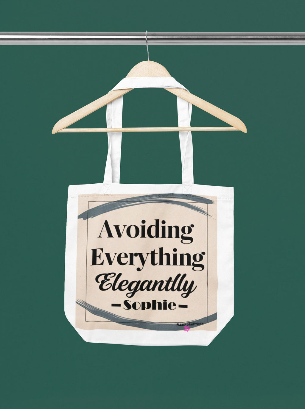 White canvas tote bag hanging, printed "Avoiding Everything Elegantly" text