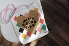 White canvas tote bag with heart logo, multicolor diamond pattern, pink handles