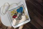 White tote bag with blue border and colorful heart graphic with text