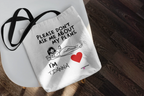 White canvas tote bag on wood with “Please don’t ask me about my plans” print and red heart
