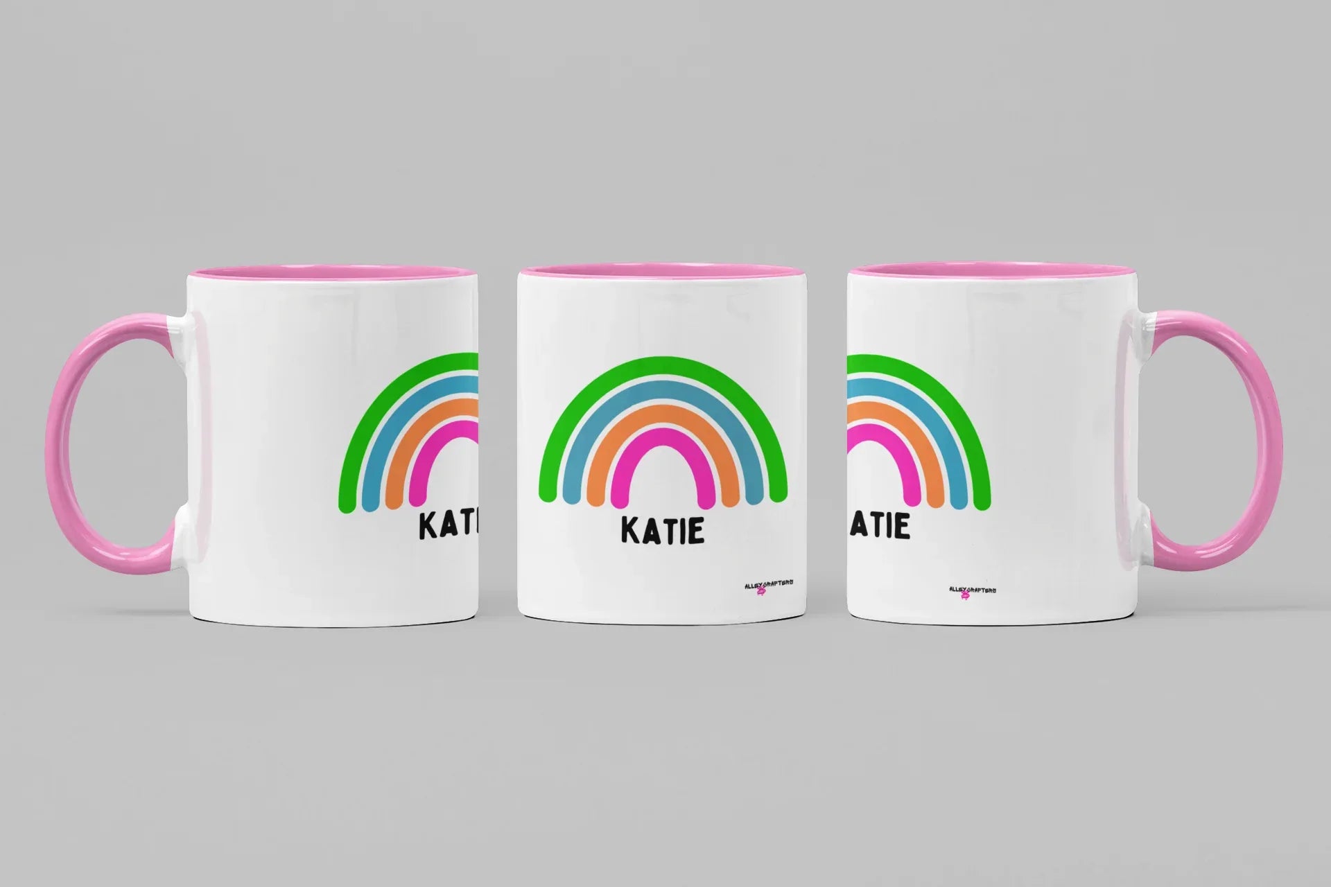 Set of three personalised rainbow mugs with name Katie, pink handles and rims.