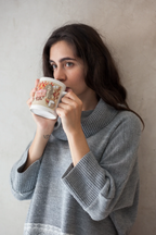 White ceramic mug with flame-haired woman graphic and coffee cup, held in gray sweater