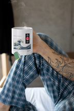 White mug with blue ocean wave print and red/black emblem, held in a hand.
