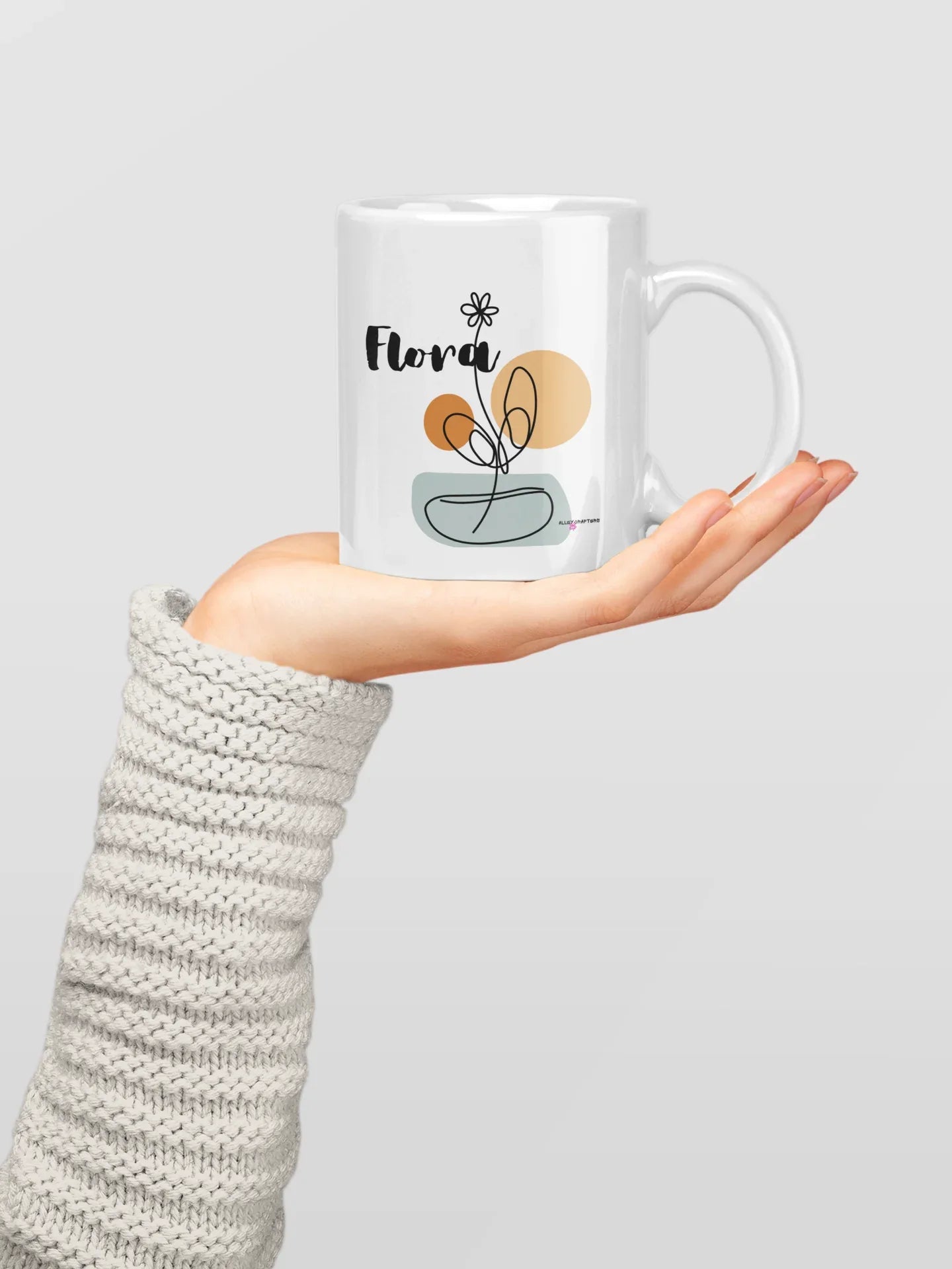 White ceramic mug with Flora name and floral pot graphic, held on a plain background