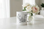 White ceramic mug with floral line art and text “SINCE 2000” on the front.