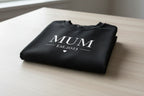 Folded personalised black sweatshirt with front text "MUM" and small Est.2023