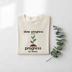 Natural/cream T-shirt with "slow progress" slogan and minimal plant graphic, crew neck.