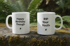 White coffee mugs outdoors on moss, printed "Happy Birthday Though" and "RIP Your Youth".