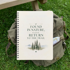 Cream nature notebook with spiral binding on grass, cover shows forest and “Return to the Trail”.