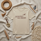 Cream T-shirt with #PROTECT THE OCEANS graphic, flat lay on a fabric surface