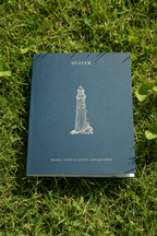Blue A5 notebook with OLIVER name and lighthouse illustration on grass.