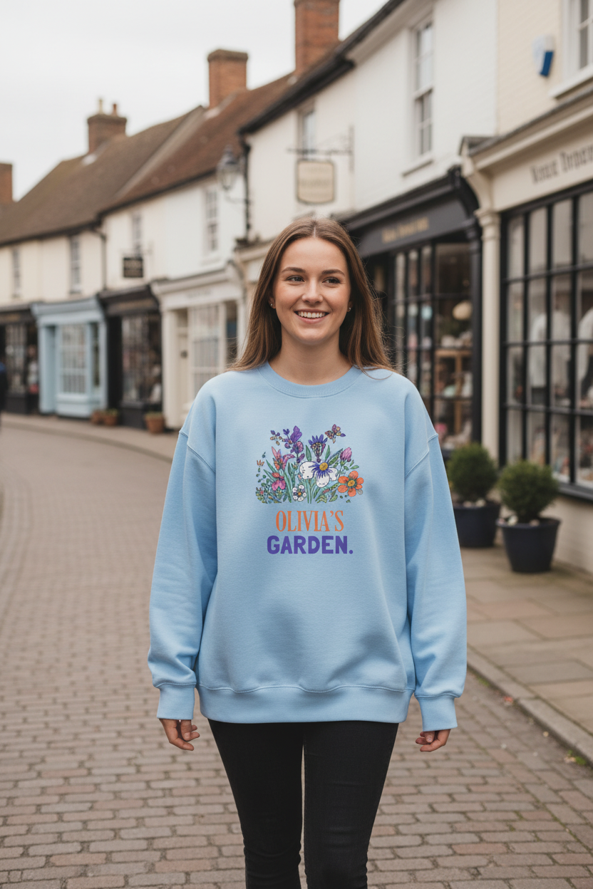 Light blue crewneck sweatshirt with floral “Olivia's Garden” name print on front