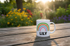 Personalised rainbow mug with name LILY and a white handle, on a wooden table.