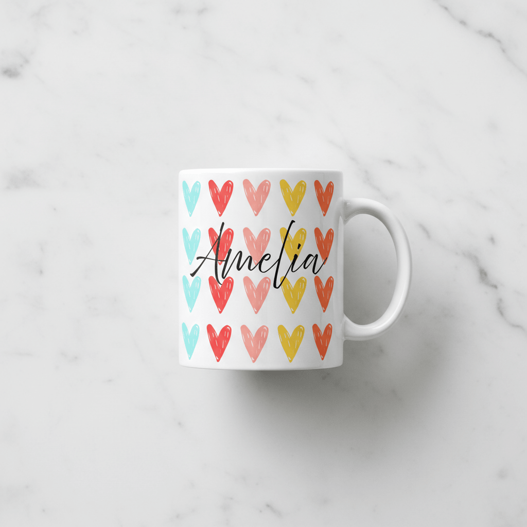 White coffee mug with colorful hearts and black cursive 'Amelia'; angled view