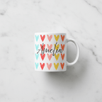 White coffee mug with colorful hearts and black cursive 'Amelia'; angled view