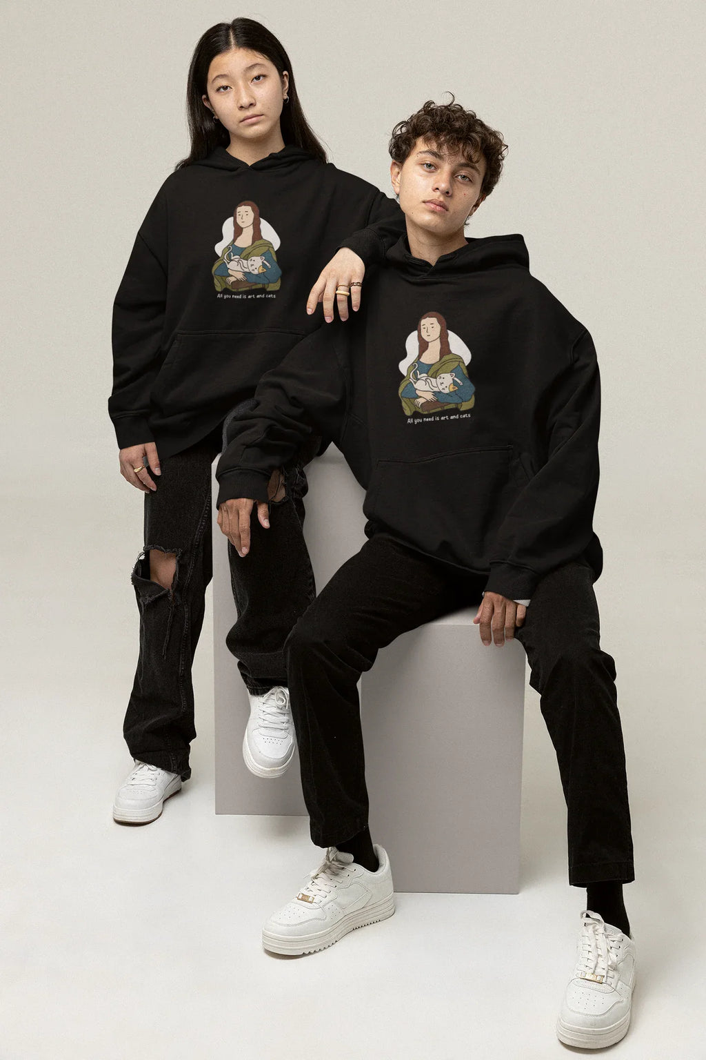 Black hoodie on two models, each with cat-and-art chest graphic