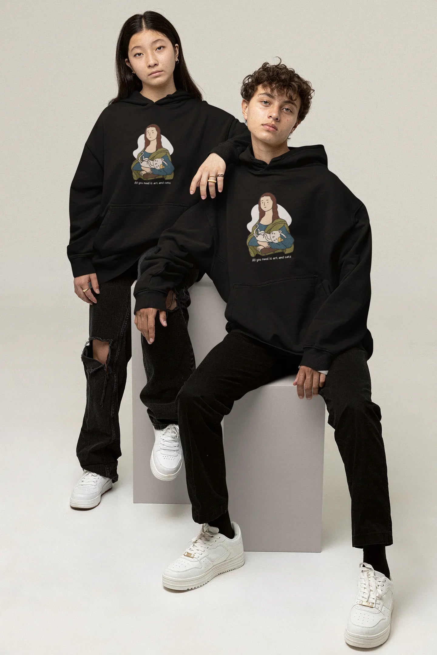 Black hoodie on two models, each with cat-and-art chest graphic