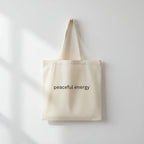 Cream cotton tote bag with long handles and 'peaceful energy' front print.