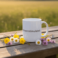 White mug with printed “Overstimulated.” on a wooden surface